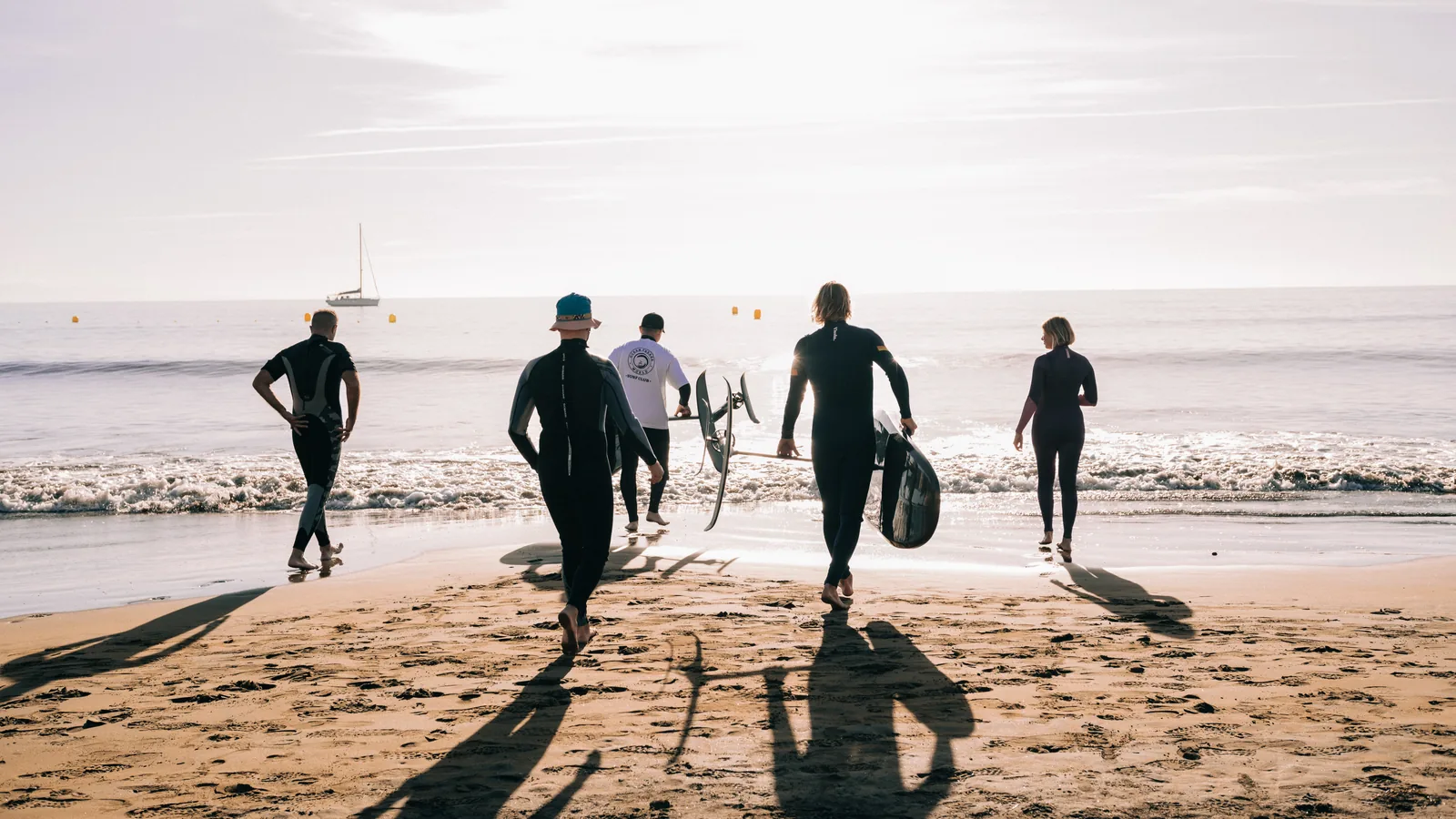 Un grupo lleva tablas de eFoil hacia el océano por una playa de arena