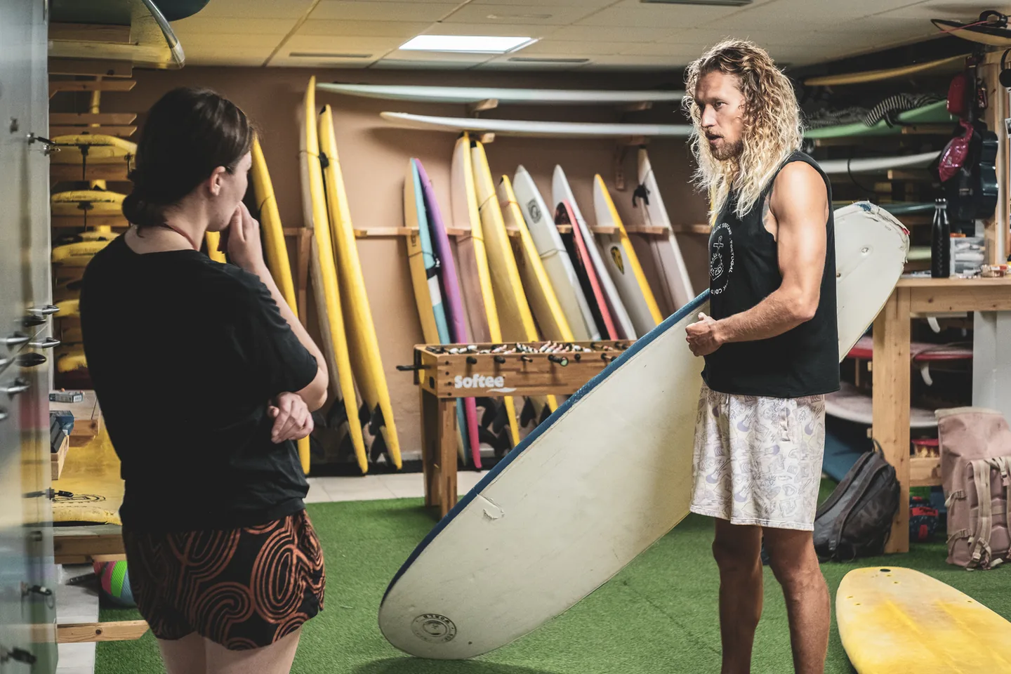 Two people discussing a surfboard beside the board racks at Ocean Freaks World.