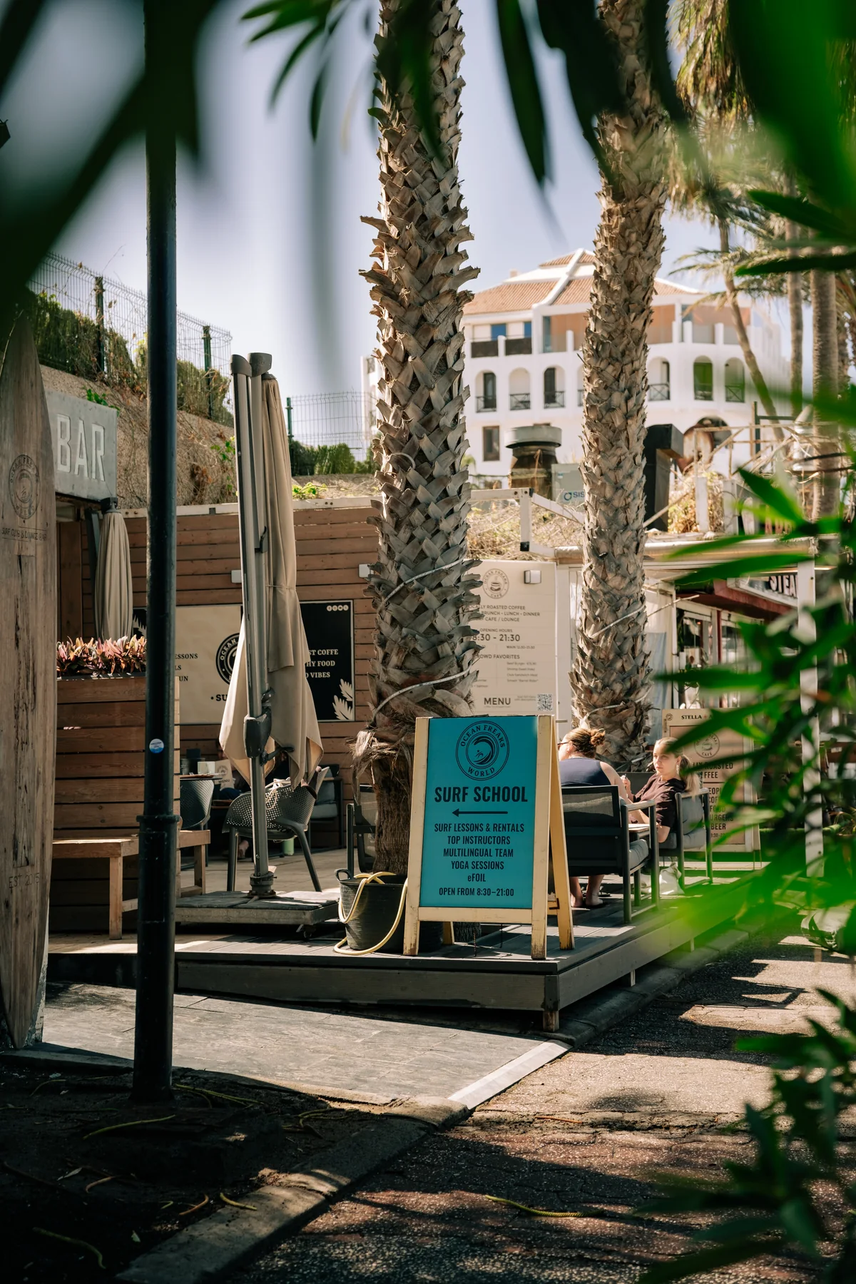 The palm-lined terrace at Ocean Freaks World, with café seating and the surf school entrance in Las Américas.